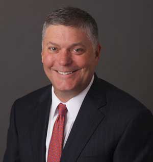 Headshot of Royce Carrigan wearing black suit with a red tie