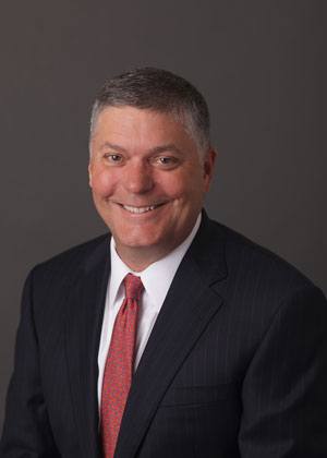 Headshot of Royce Carrigan wearing black suit with a red tie