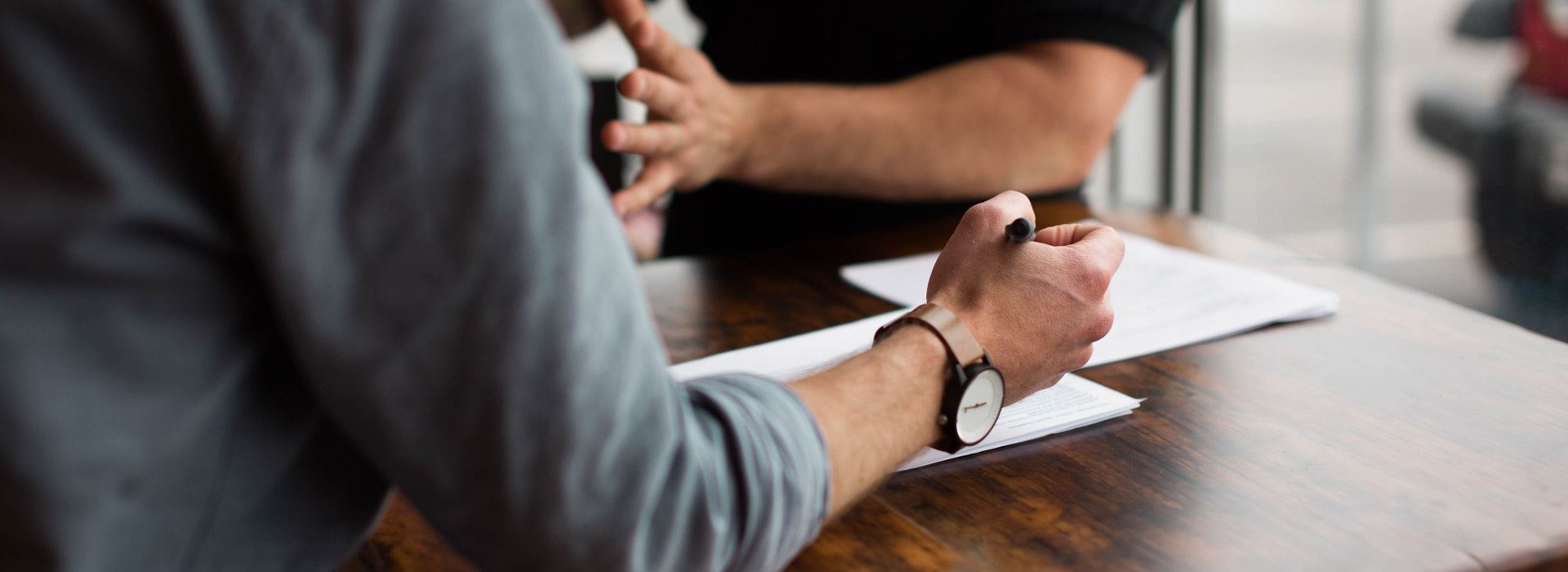 Two men in business casual attire are reviewing documents with a pen